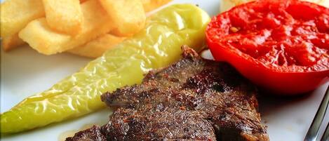 A plate with grilled steak, French fries, a slice of tomato, and a green chili pepper.