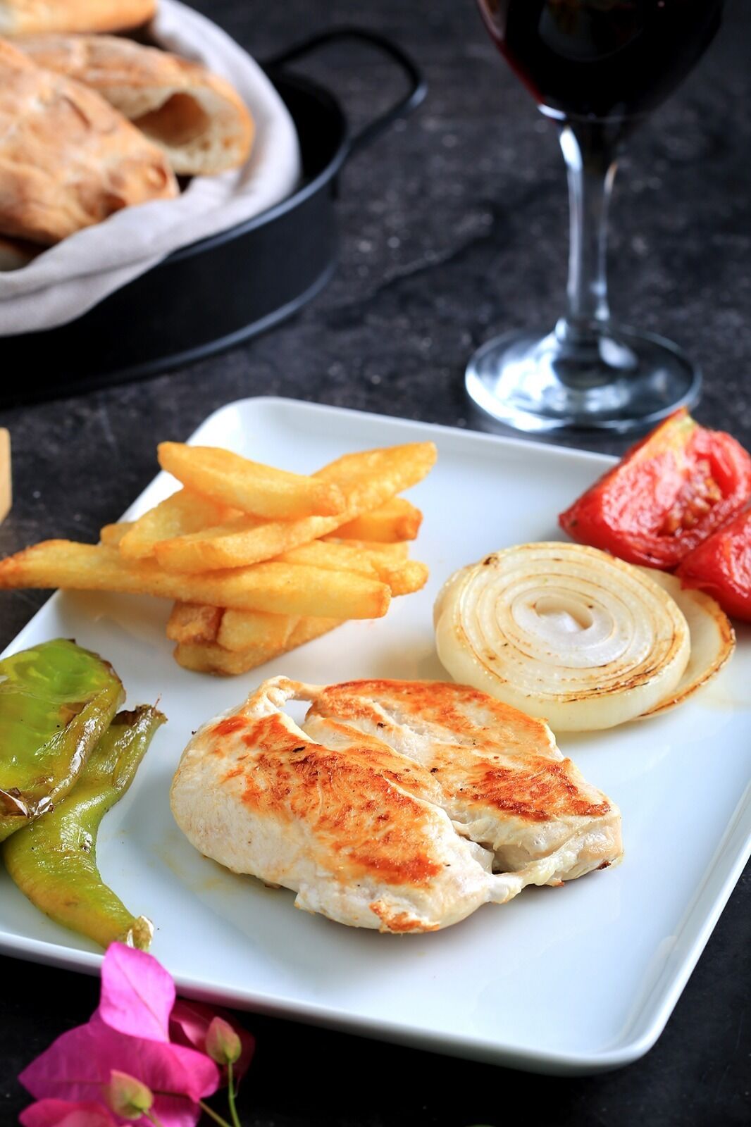 A plate with grilled chicken, French fries, pickles, and a red pepper.