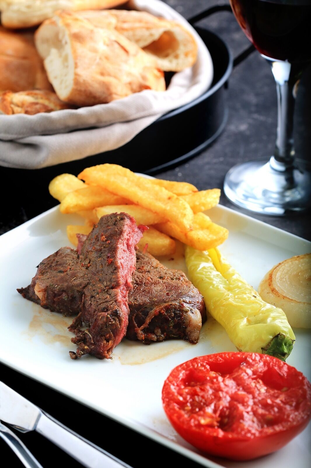 Un plato con bistec, papas fritas, un pimiento a la parrilla y un tomate.