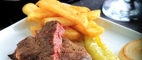 Un plato con bistec, papas fritas, un pimiento a la parrilla y un tomate.