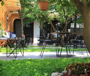 Un espace extérieur aménagé avec des tables et des chaises, entouré de verdure et bordé d’un bâtiment à la façade en bois.