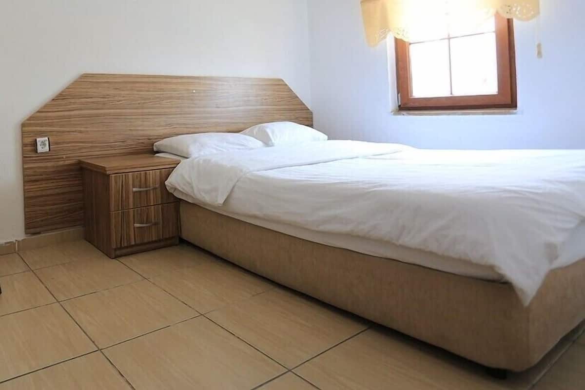 A bedroom with a bed, a nightstand, a window with a curtain, and a tiled floor.
