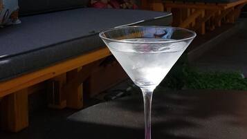 Una copa de martini con líquido transparente sobre una mesa redonda, acompañada de flores rosadas.