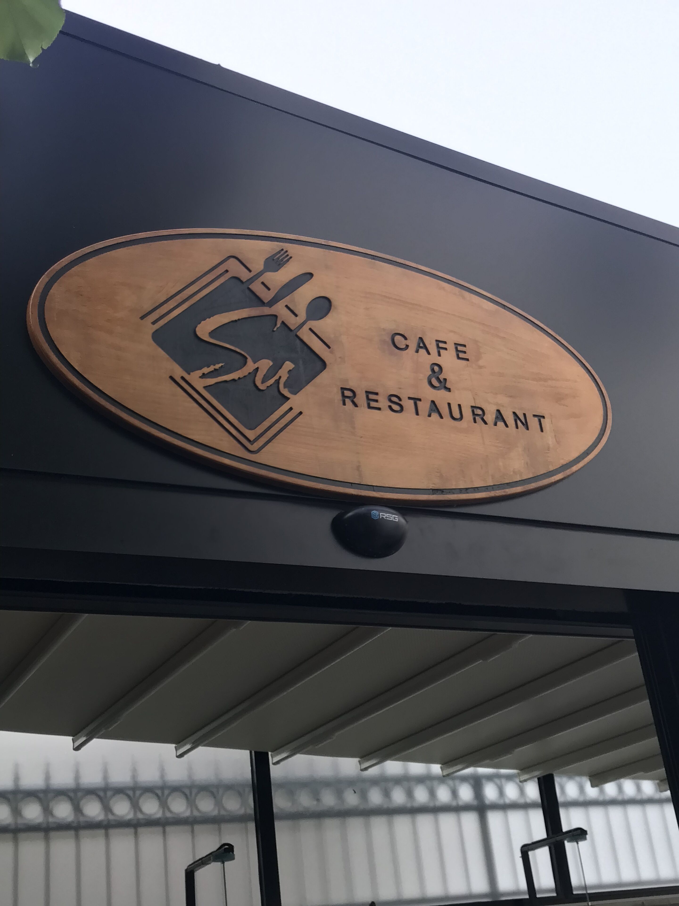 A sign for a cafe and restaurant with a logo featuring a cup and spoon.