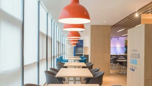 A modern dining area with multiple tables and chairs, red pendant lights, and a view of the kitchen area in the background. - Holiday Inn Express Hangzhou Jiuzhou by IHG (Hangzhou)