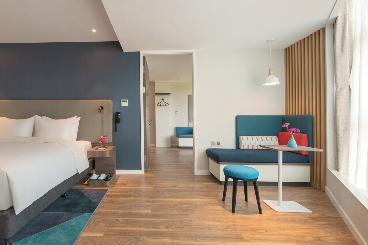 Een moderne hotelkamer met een bed, een bureau, een stoel en uitzicht op de gang.
