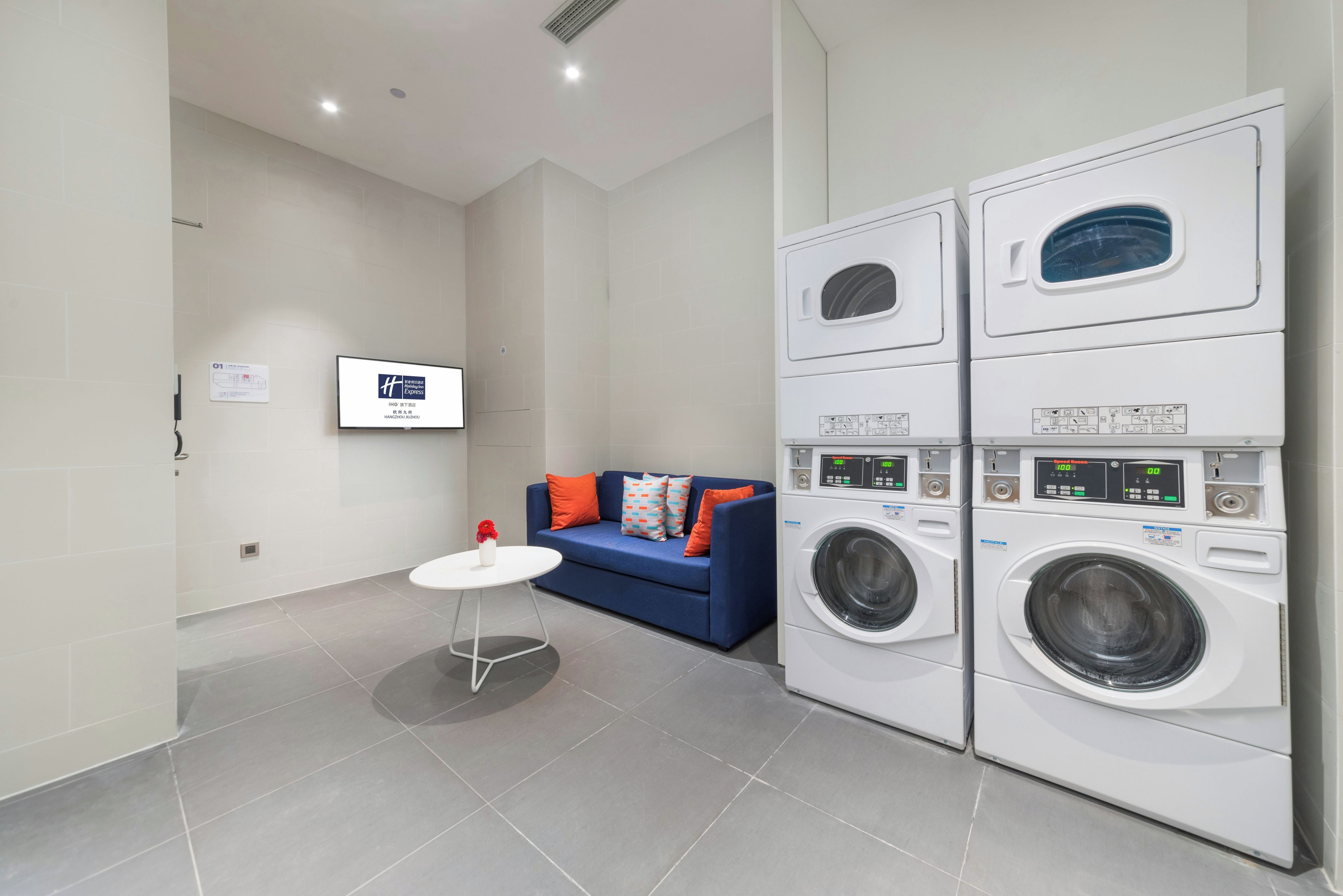 A laundry room with stacked washing machines and a blue sofa with orange cushions.