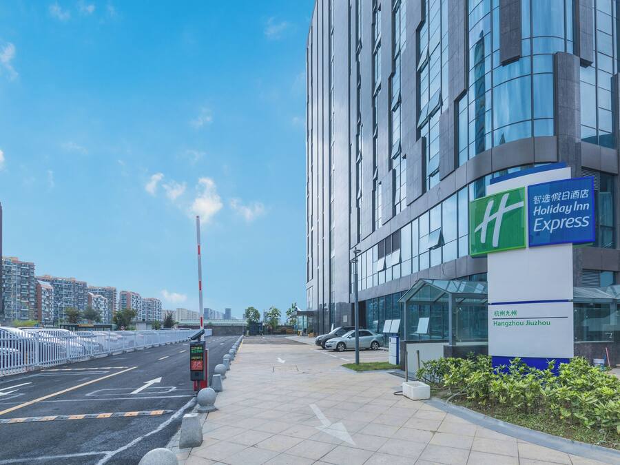 Exterior moderno de um hotel com céu claro, placa Holiday Inn Express e área de estacionamento fechada por portão.