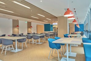 A modern dining area with multiple tables and chairs, overhead lighting, and a kitchen area in the background. - Holiday Inn Express Hangzhou Jiuzhou by IHG (Hangzhou)