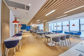 A modern dining area with tables and chairs, a kitchen area, and large windows. - Holiday Inn Express Hangzhou Jiuzhou by IHG (Hangzhou)