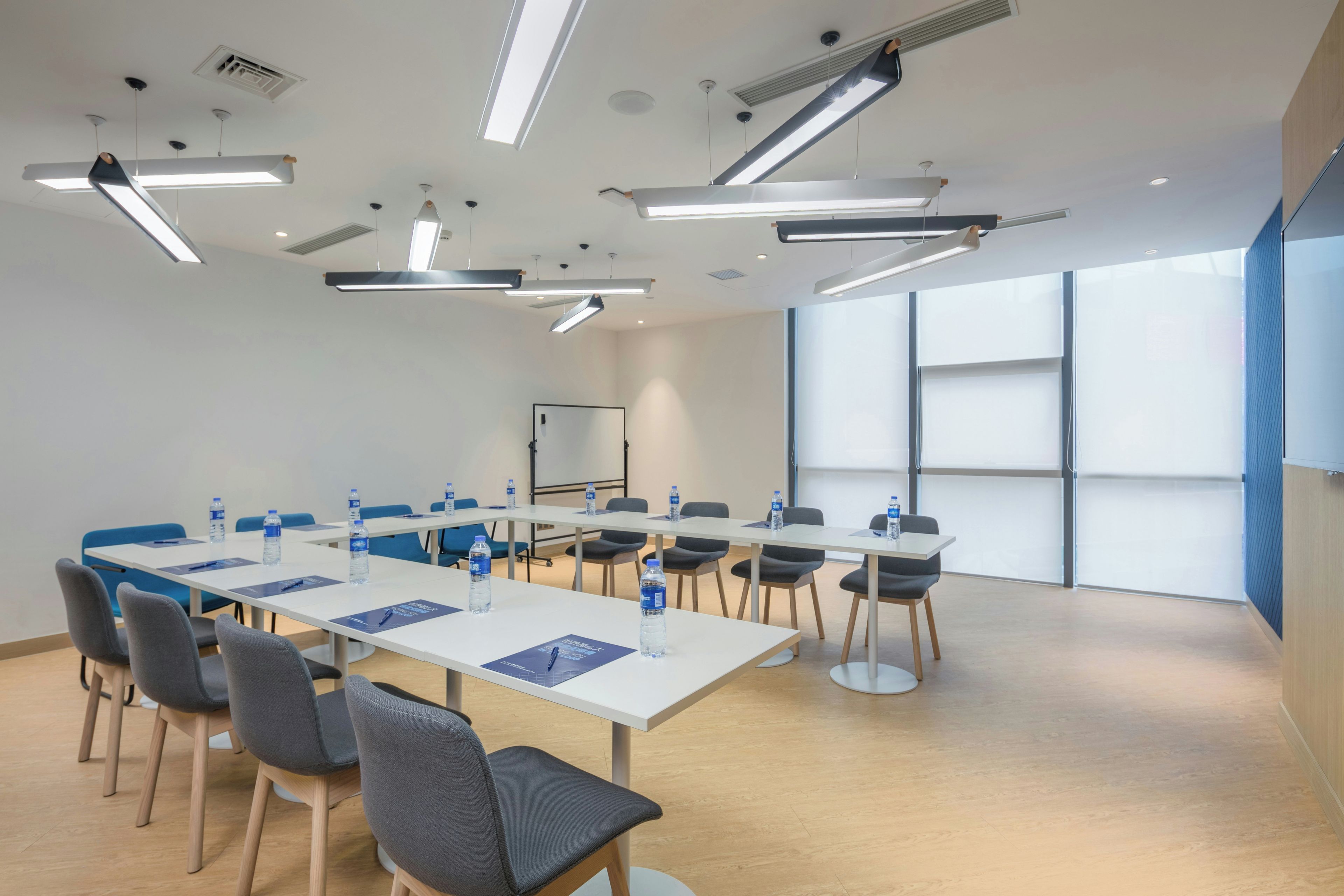 A conference room with a long table, chairs, water bottles, and a projector screen.