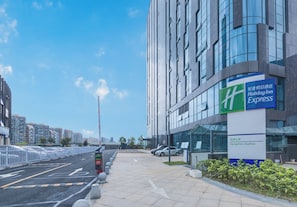 Een modern hotelgebouw met een heldere lucht, een Holiday Inn Express bord en een afgesloten parkeerterrein.