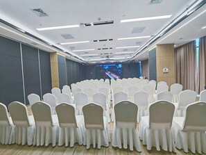 Ein Konferenzraum mit Reihen weißer Stühle, einer Bühne mit einer großen Leinwand und einem Holzboden.