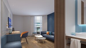 A modern hotel room with a sofa, a coffee table, a TV, and a bathroom with a mirror and sink. - Holiday Inn Express Hangzhou Jiuzhou by IHG (Hangzhou)