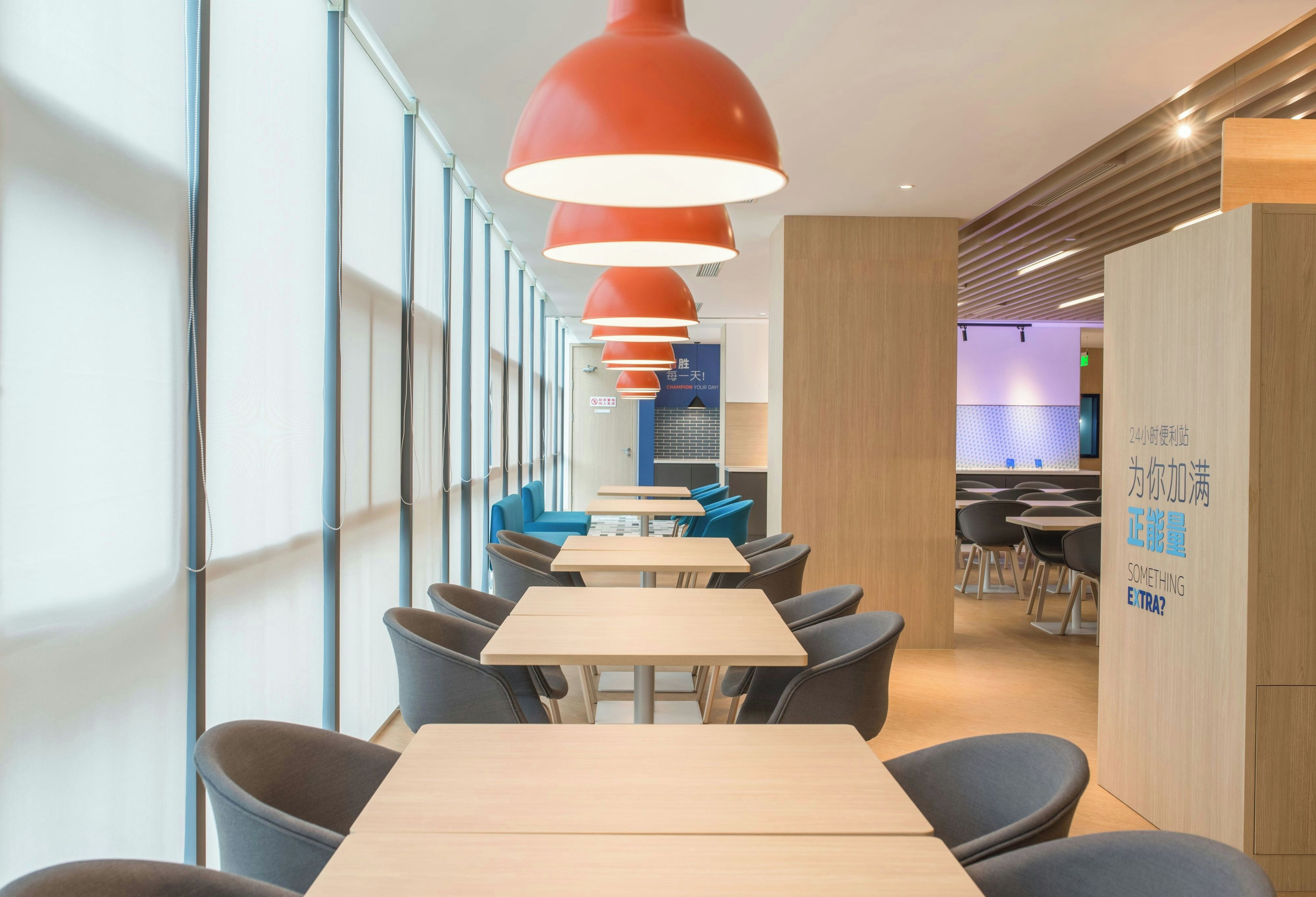 A modern interior with long tables and chairs, red pendant lighting, and a visible sign with text.