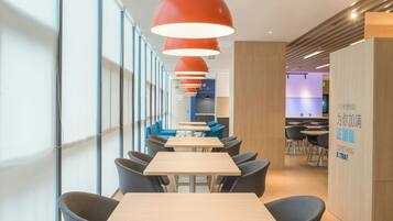 A modern interior with long tables and chairs, red pendant lighting, and a visible sign with text.