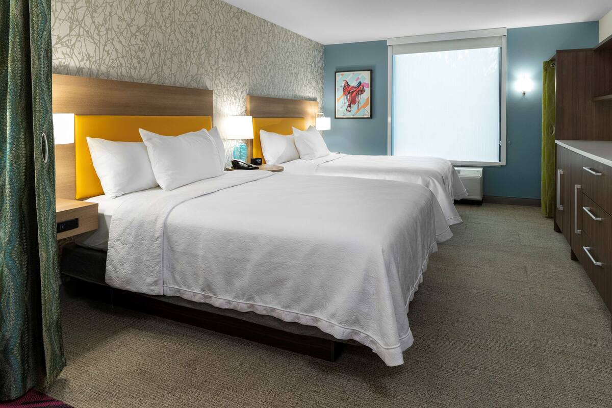 Habitación de hotel con dos camas, un cabecero de madera, un ventanal grande y una obra de arte colgada en la pared.
