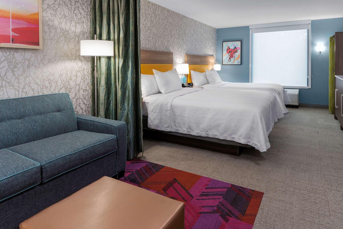 Una habitación de hotel con un sofá, dos camas, un escritorio y una alfombra estampada.