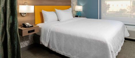 A neatly made hotel room with a large bed, two bedside lamps, a nightstand with a phone, and a window with a view of a building.