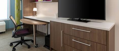 Een hotelkamer met een flatscreen televisie, een bureau met stoel, een lamp en een kledingkast.