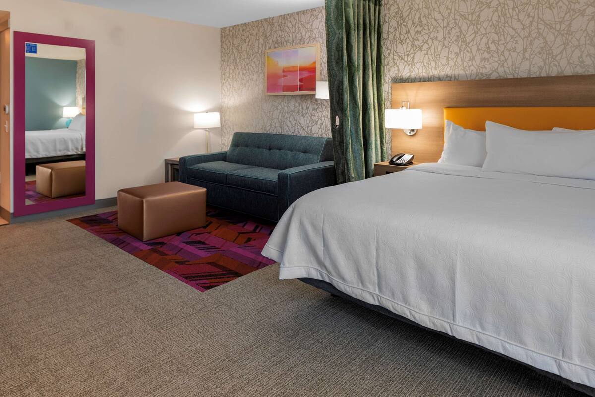 Una habitación de hotel con una cama, un sofá, una silla, una mesita y un espejo.