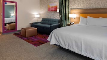 A hotel room with a bed, a sofa, a chair, a small table, and a mirror.