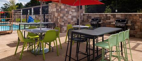 Un patio al aire libre con mesas y sillas, una parrilla y una piscina al fondo.