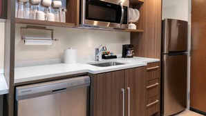 Una cocina moderna con electrodomésticos de acero inoxidable, armarios de madera y encimera blanca.