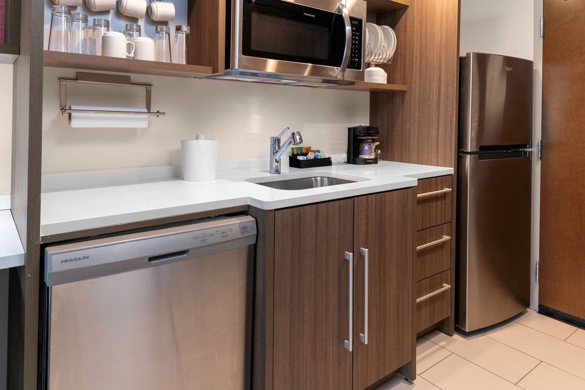 Una cocina moderna con electrodomésticos de acero inoxidable, armarios de madera y encimera blanca.