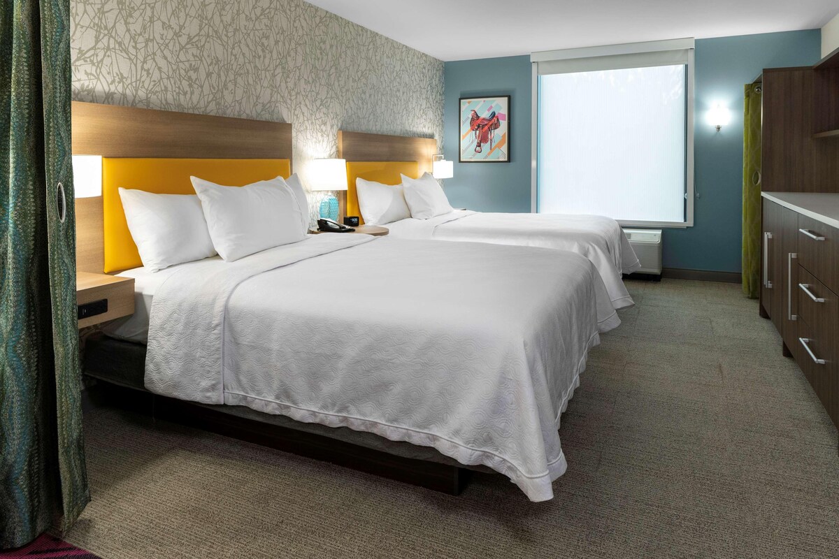 Habitación de hotel con dos camas, cabecero de madera, un ventanal grande, un cuadro en la pared y un minibar.