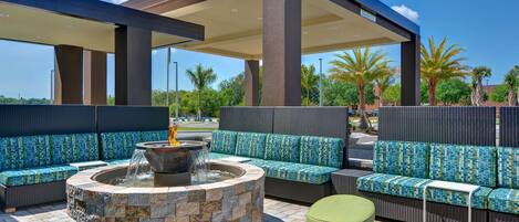 An outdoor seating area with a fire pit, cushioned seating, and a covered patio.