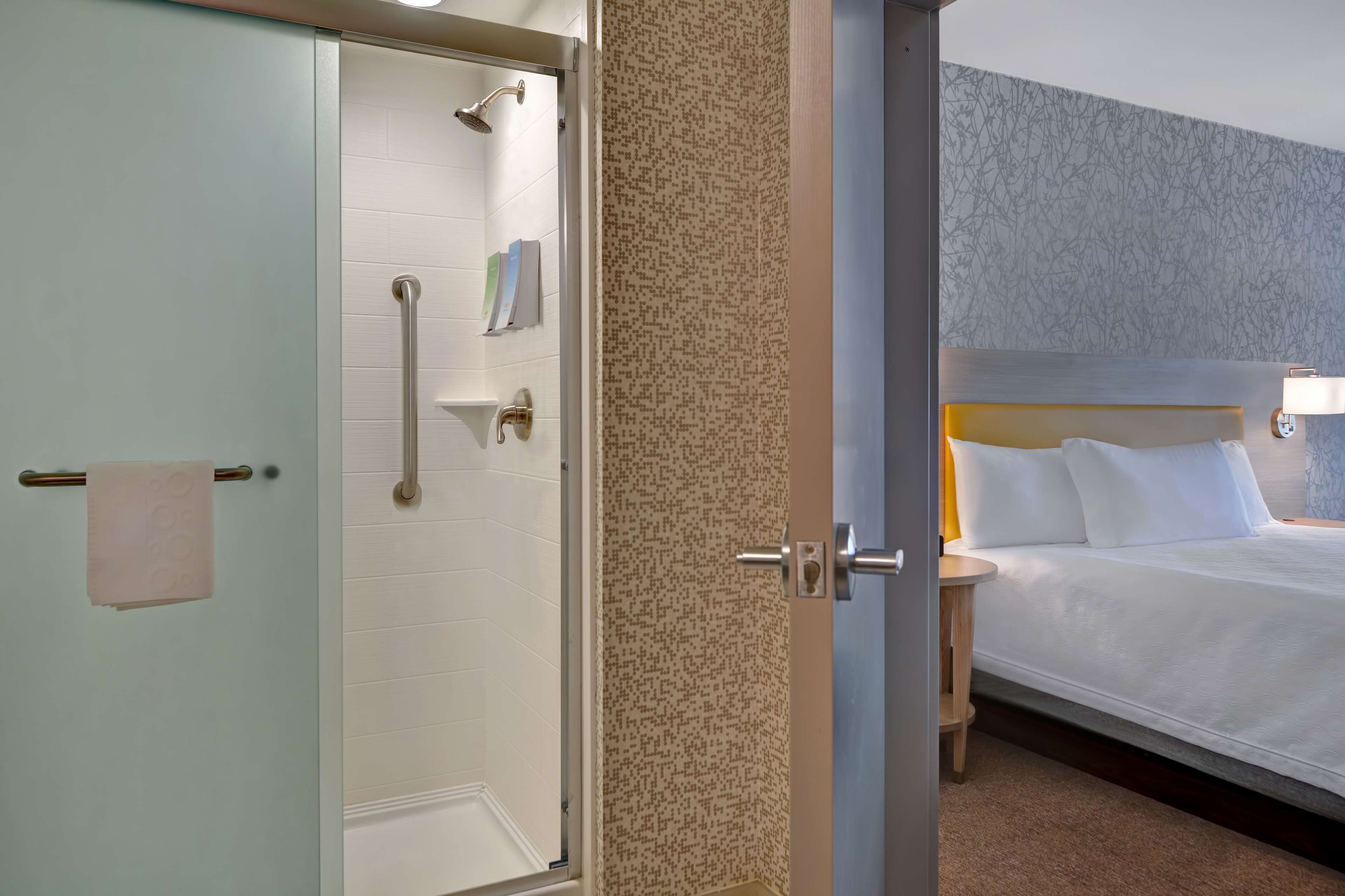 Une chambre d’hôtel avec une douche, un lit avec du linge de lit blanc, une table de chevet avec une lampe et un mur décoré d’un motif.