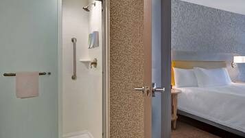 Une chambre d’hôtel avec une douche, un lit avec du linge de lit blanc, une table de chevet avec une lampe et un mur décoré d’un motif.