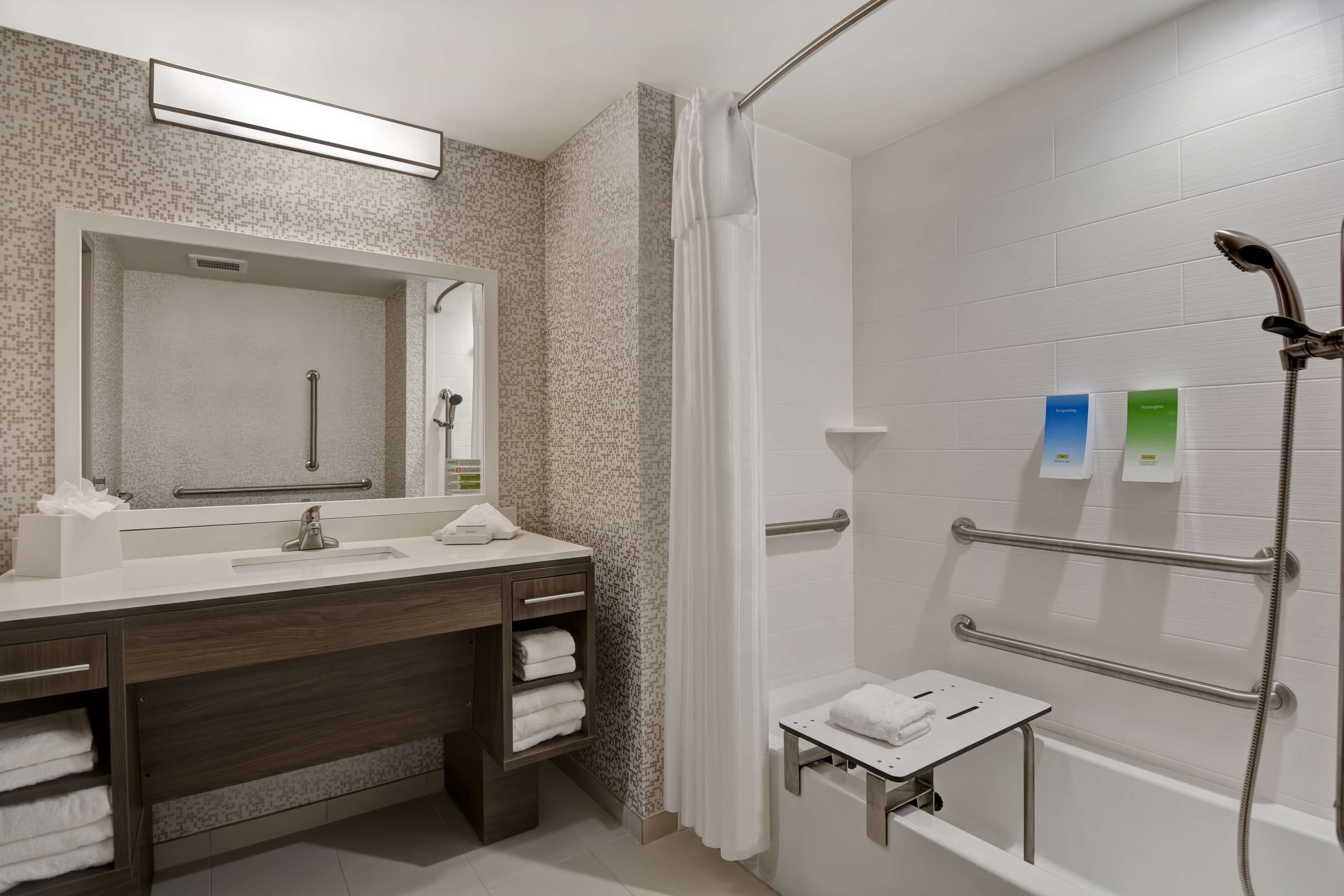 A modern bathroom with a shower, a vanity with a mirror, and a small table with towels.
