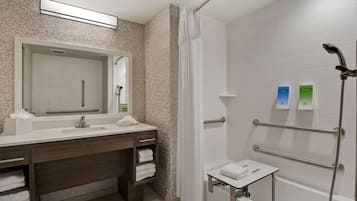 A modern bathroom with a shower, a vanity with a mirror, and a small table with towels.