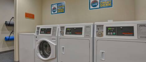 A laundry area with four front-loading washing machines, a blue yoga mat, and two signs on the wall.