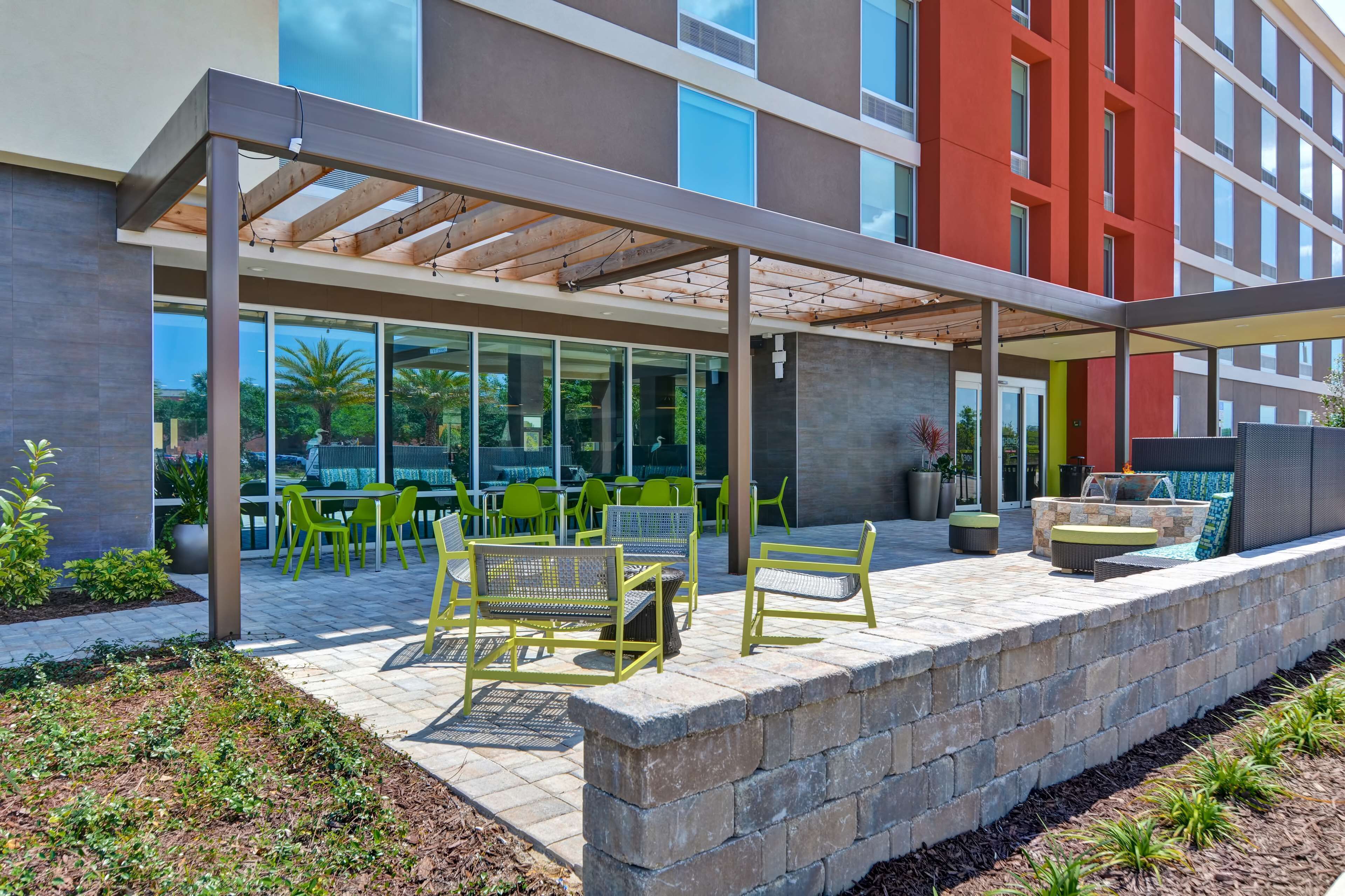 An outdoor patio area with seating and a covered section, adjacent to a building with large windows and a red facade.
