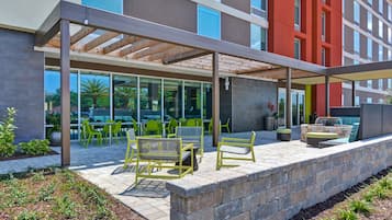 An outdoor patio area with seating and a covered section, adjacent to a building with large windows and a red facade.