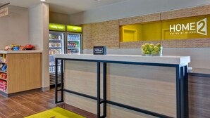 A hotel reception area with a counter, a minibar, and a refrigerator displaying 'really cold' and 'cold' signs. - Home2 Suites Sarasota I-75 Bee Ridge, FL (Sarasota)