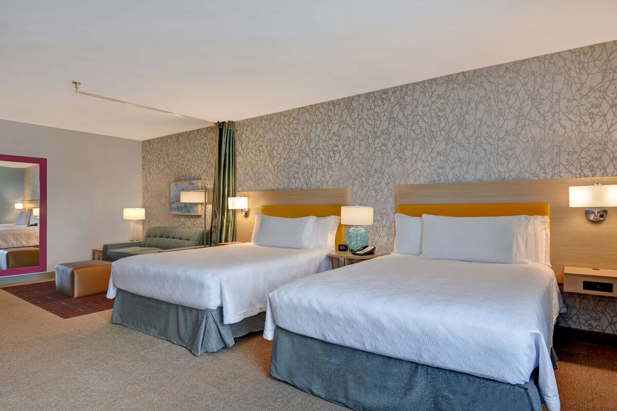 A hotel room with two beds, a sofa, a mirror, and a nightstand with a lamp.