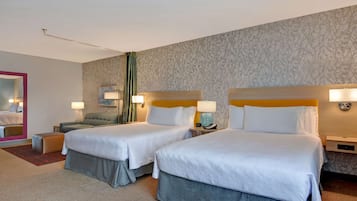 A hotel room with two beds, a sofa, a mirror, and a nightstand with a lamp.