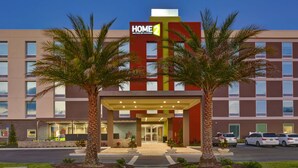 A hotel entrance with a red and yellow sign, palm trees, and a parking lot. - Home2 Suites Sarasota I-75 Bee Ridge, FL (Sarasota)