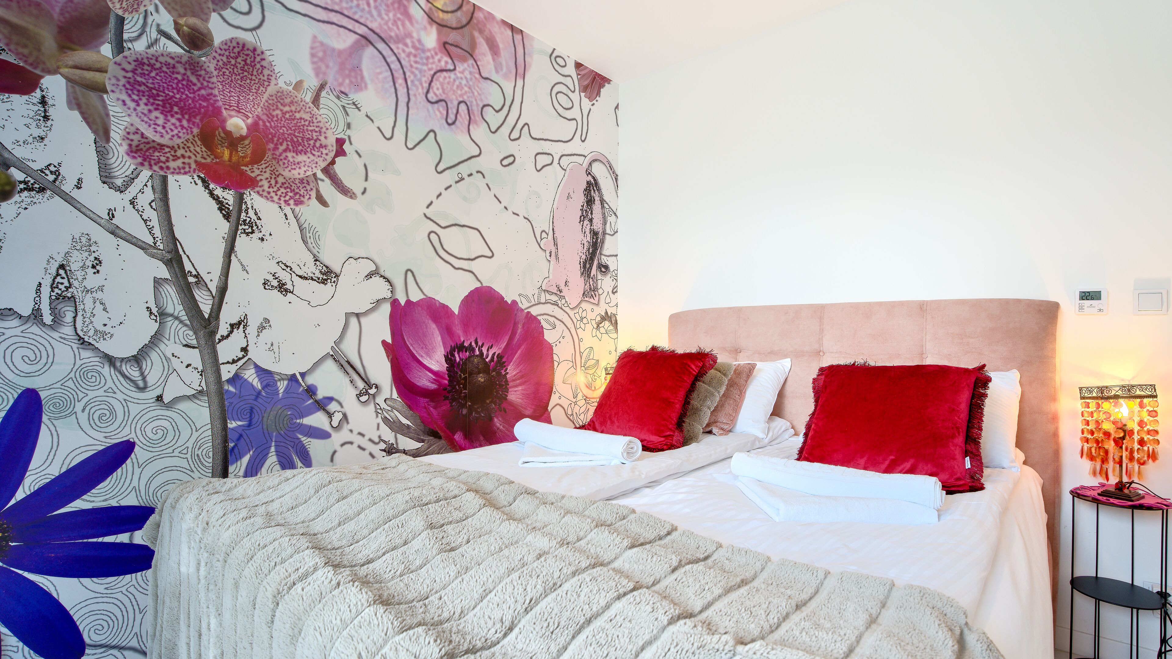 Ein Schlafzimmer mit einem Bett, Kissen, einem Nachttisch und einer Wand mit floralen Bildern.