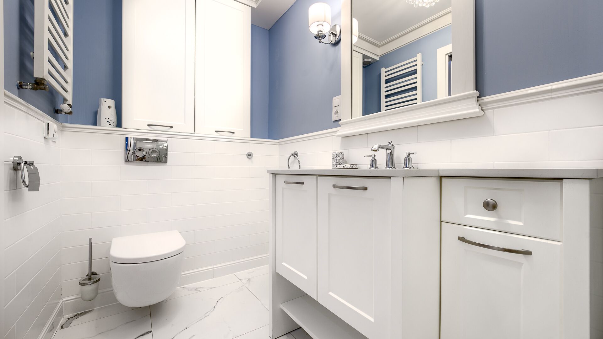 A modern bathroom with white cabinetry, a white toilet, and a blue accent wall.