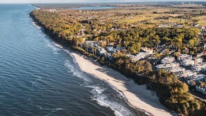 Eine Vogelperspektive auf eine Küstenstadt mit Strand, Häusern und Windkraftanlagen in der Ferne.