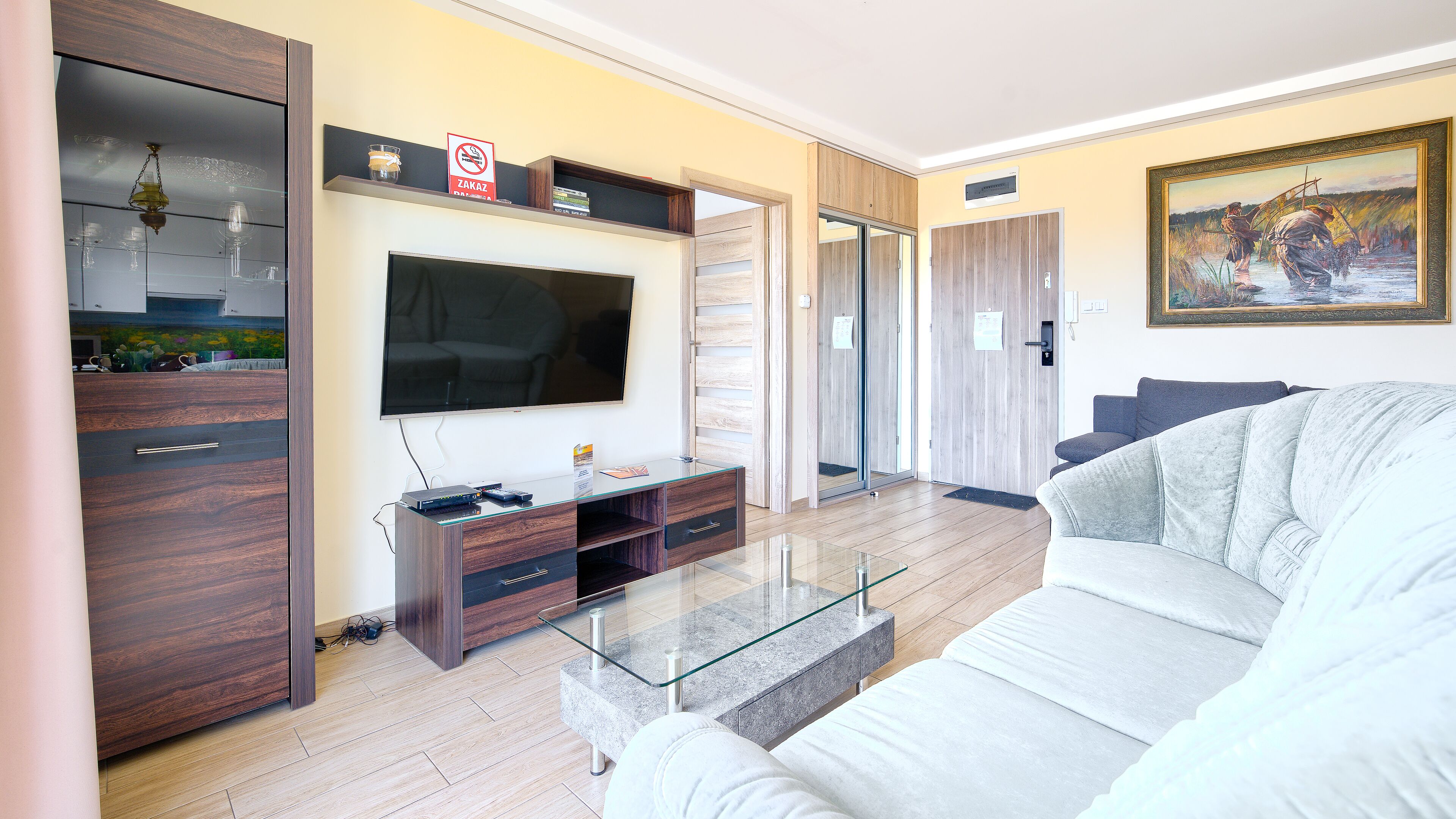 Una sala de estar moderna con una televisión de pantalla plana, armarios de madera, una mesa de centro de vidrio y un sofá gris.