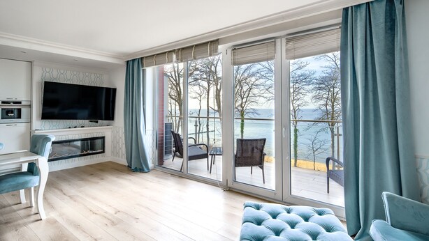 Ein modernes Wohnzimmer mit Flachbildfernseher, Kamin und einer großen Schiebeglastür, die auf einen Balkon mit Meerblick führt.