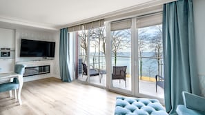 Un salon moderne doté d’un téléviseur à écran plat, d’une cheminée et d’une grande porte-fenêtre coulissante donnant sur un balcon avec vue sur la mer.