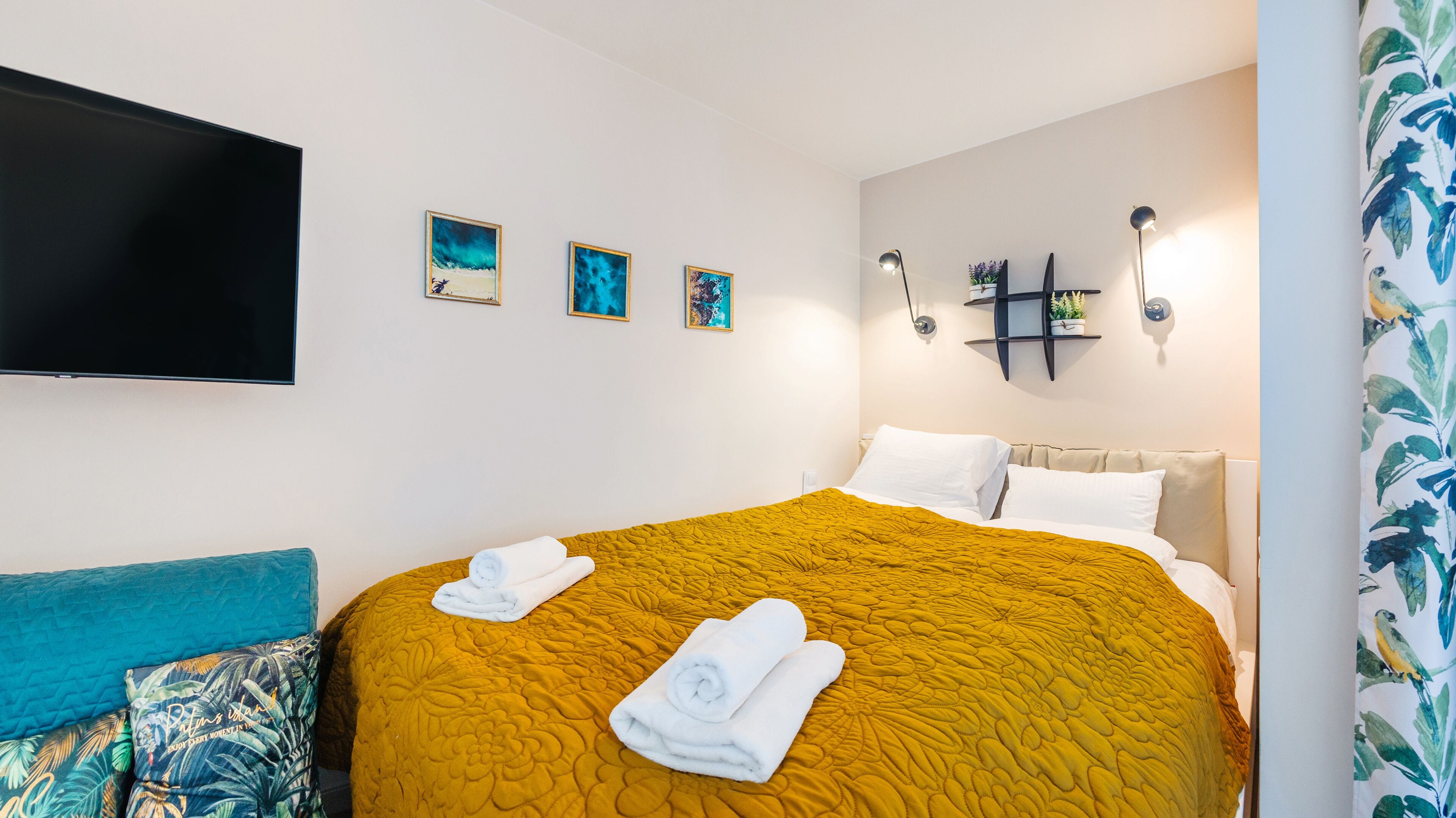 Une chambre d’hôtel avec un grand lit, un téléviseur à écran plat fixé au mur et trois œuvres d’art encadrées au-dessus du lit.