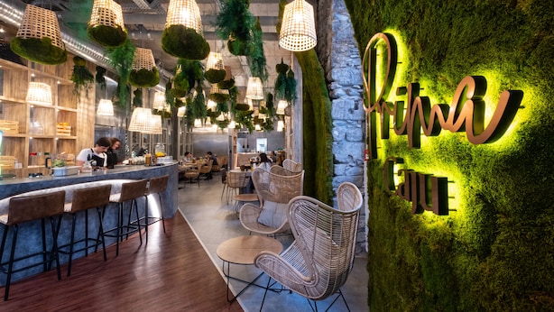 A modern restaurant interior with hanging green plants, wicker furniture, and a neon sign on the wall. - Hotel Caju (Funchal)